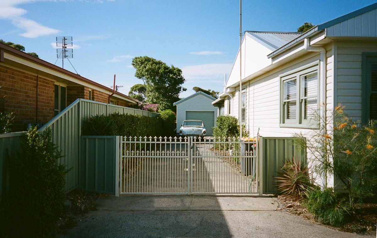 A residential front fence with three different gate setups shown side by side: a sliding gate stacked back along the fence line, a double swing gate opening inward across a level driveway, and a cantilever gate suspended above the entrance without a ground track